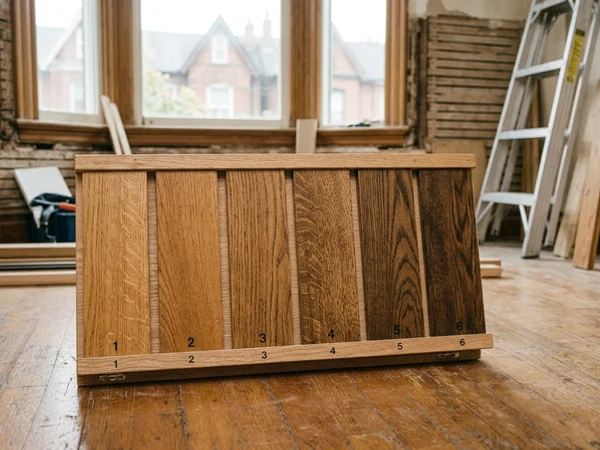 Stain sample boards on quarter-sawn oak held against a hardwood floor